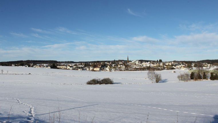 Un paysage enneigé avec un petit village à l'arrière-plan. Le ciel est clair et bleu.