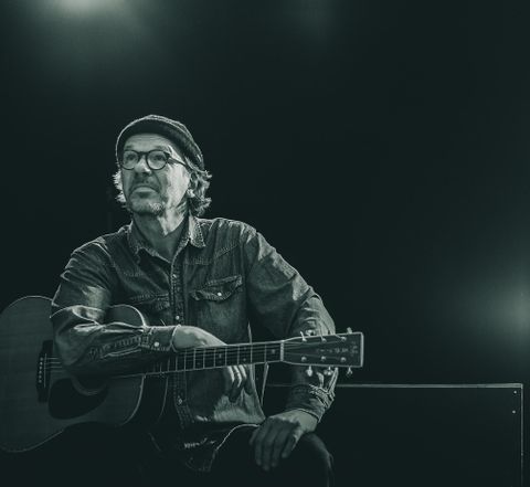 Un musicien pensif est assis avec une guitare. La scène est en noir et blanc et transmet une atmosphère créative.
