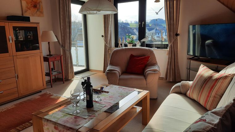 Un salon confortable avec un canapé lumineux et un fauteuil. De grandes fenêtres offrent une vue sur le paysage.