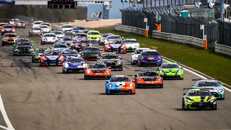 Eine Vielzahl von Rennwagen startet auf der Rennstrecke. Bunte Autos rasen in voller Geschwindigkeit in Richtung Kurve.