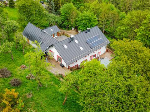 Een modern huis omringd door groene bomen. De tuin is mooi aangelegd met een terras.
