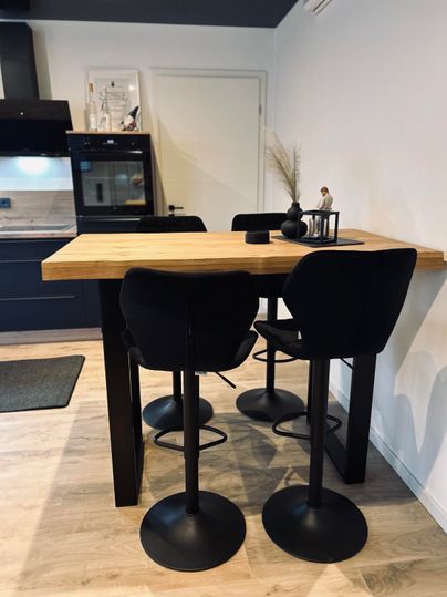 A modern dining area with a wooden table and black bar stools. The kitchen in the background is stylish and well-equipped.