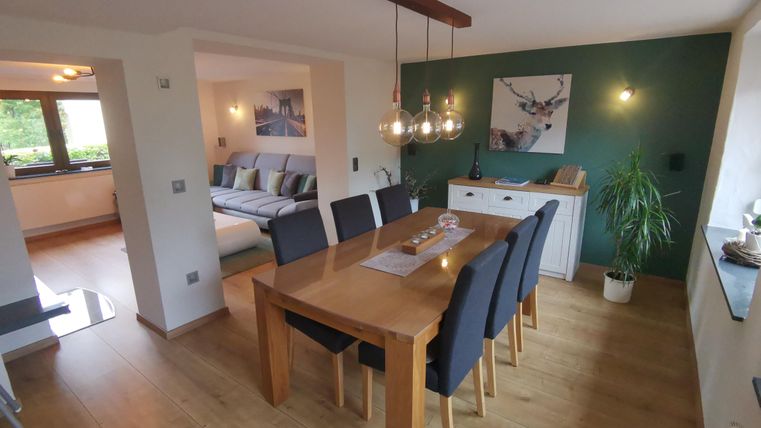 A modern dining room with a wooden desk and black chairs. The walls are in soft colors, and there is attractive decoration.
