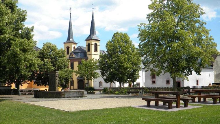 Dorfplatz mit Kirche und Bäumen in Idenheim.