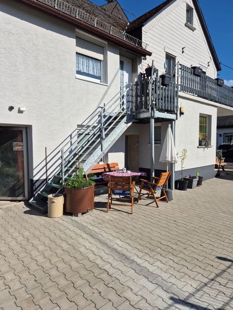 Eine gemütliche Terrasse mit einem Tisch und Stühlen. Die Treppe führt zu einem oberen Balkon eines Hauses.