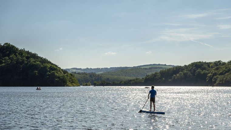 See im Sonnenlicht mit einem Mann beim Stand-Up-Paddling