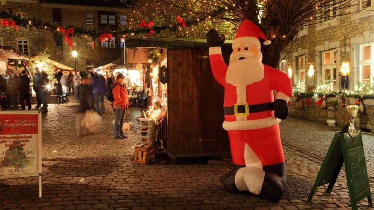 Ein festlich dekorierter Weihnachtsmarkt mit einem großen aufblasbaren Weihnachtsmann. Lichter und festliche Stände schaffen eine gemütliche Atmosphäre.