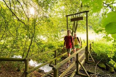 Zwei Wanderer überqueren eine Holzbrücke im Wald.