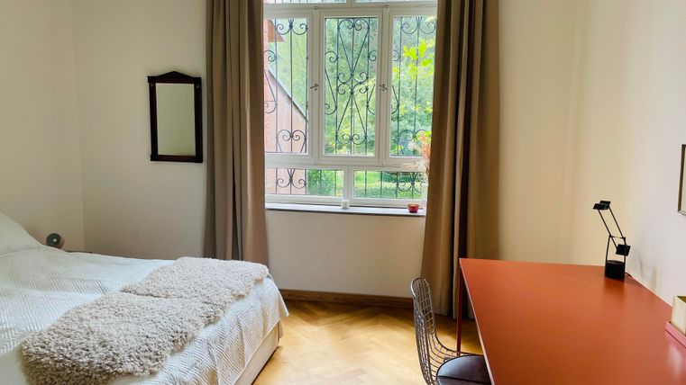 Une chambre lumineuse avec un lit et un bureau. De grandes fenêtres laissent entrer beaucoup de lumière du jour.
