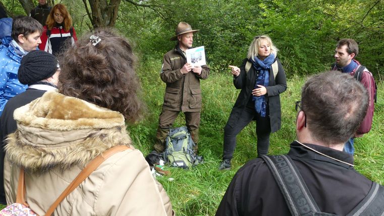 <p>Ein Ranger erklärt der Gruppe etwas und zeigt es auf Bildern. Die Dolmetscherin übersetzt in Zeichensprache.</p>