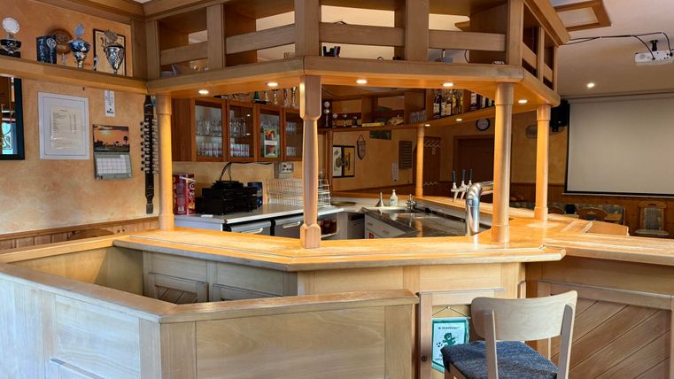 Een gezellige houten bar met barkrukken en een goed uitgeruste bar. De ruimte heeft een uitnodigende sfeer.