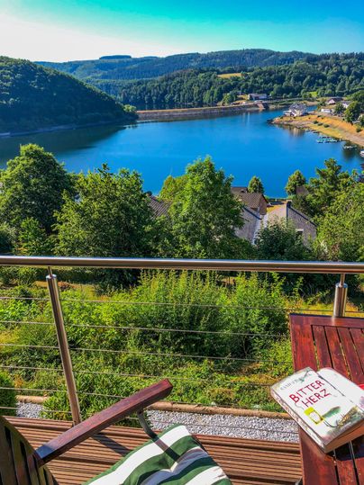 Une belle vue sur un lac clair entouré d'arbres. Sur une table se trouve un livre qui invite à la détente.