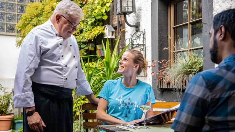 Un cuisinier parle à une femme souriante dans le jardin d'un restaurant.