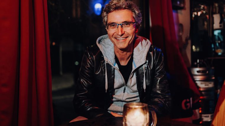 Ein Mann mit Brille sitzt in einer Bar mit einem Bierkrug.