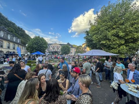 Een prachtige tuin met kleurrijke bloemen in rood, geel en blauw. Op de achtergrond is een elegant gebouw met decoratieve ramen en planten te zien.
