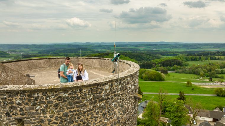Une famille se tient en haut d'une tour avec vue sur le paysage verdoyant de l'Eifel.