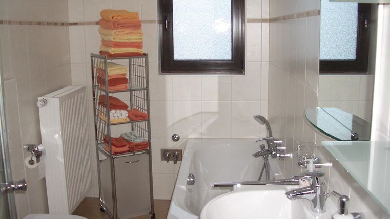 Une salle de bain moderne avec une baignoire, un lavabo et des toilettes. Sur une étagère, plusieurs serviettes sont soigneusement empilées.