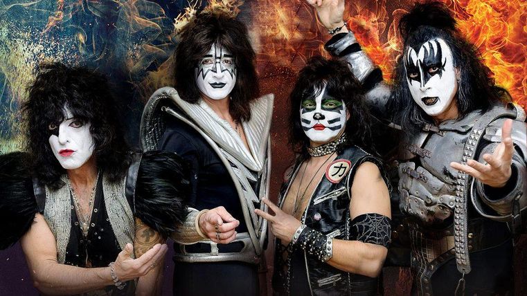 Eine Rockband mit auffälligem Make-up und extravaganten Kostümen. Die Mitglieder posieren dynamisch vor einem farbenfrohen Hintergrund.