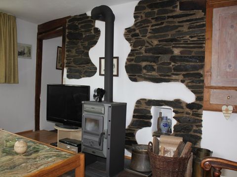 Een gezellige woonkamer met een houtkachel en een stenen muur. Op de achtergrond staat een televisie en er zijn rustieke meubels.