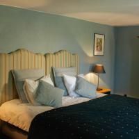 A cozy bedroom with a large bed and stylish pillows. The walls are painted in soft blue and pastel tones, and a bedside table with a lamp stands next to the bed.