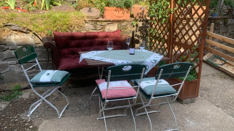 A cozy seating area in the garden with a bench and a table. Around the table are four folding chairs with checkered cushions.