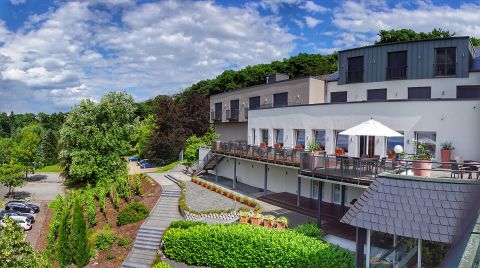 Ein modernes Gebäude mit einer Terrasse und einem großen Garten. Der Himmel ist blau mit einigen Wolken.
