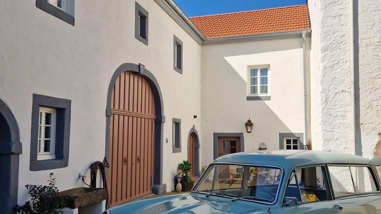 A classic mint green car is parked in front of a charming, bright building. The sky is clear and blue, creating an inviting atmosphere.