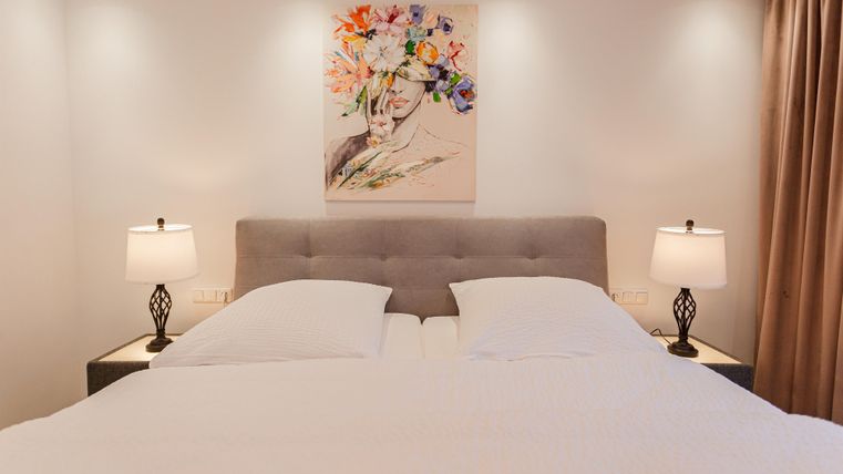 A modern bedroom with a large bed and two nightstands. A painting of colorful flowers hangs on the wall.