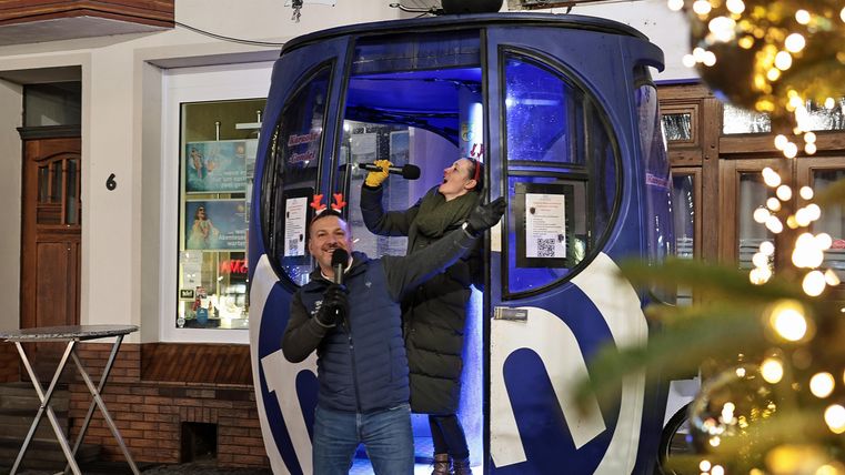 Een feestelijke scène met twee mensen die vanuit een gondel poseren. De omgeving is verlicht en zorgt voor een vrolijke sfeer.