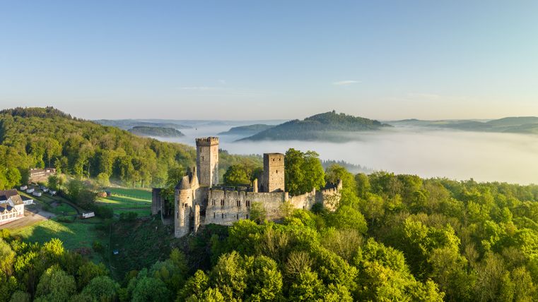 Aerial view of Kasselburg Castle in Pelm, surrounded by green forests and fog in the distance.