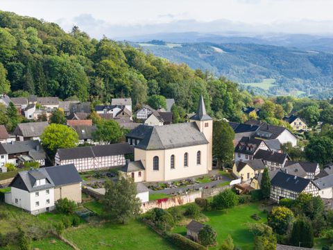 Een pittoresk dorp met een kerk en traditionele huizen. Omgeven door groene heuvels en bomen.