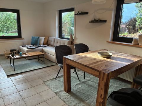 A cozy living space with a modern sofa and a wooden table. Large windows let in plenty of daylight and offer a view of the outside.