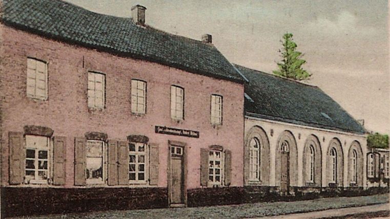 Un vieux bâtiment charmant avec une façade rose et de nombreuses fenêtres. À côté, se trouve une autre annexe avec des fenêtres rondes et un toit sombre.