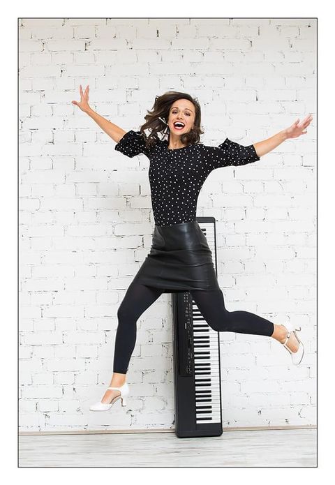 Une femme joyeuse saute avec un large sourire. À côté d'elle se trouve un clavier devant un mur de briques blanches.