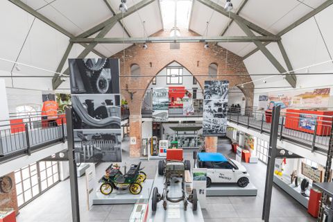 Een modern museum met historische voertuigen en grote wandmuurschilderingen. De ruimte heeft hoge plafonds en een open architectuur.