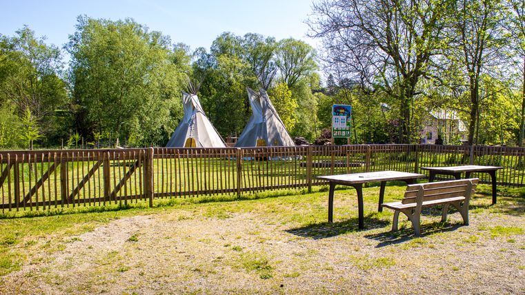 Aire de jeux avec tipis et clôture en bois, entourée d'arbres.