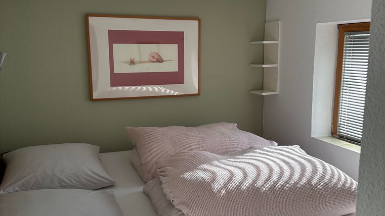 A cozy bedroom with a large bed and bright bedcovers. The walls are painted in soft colors, and a picture hangs on the wall.