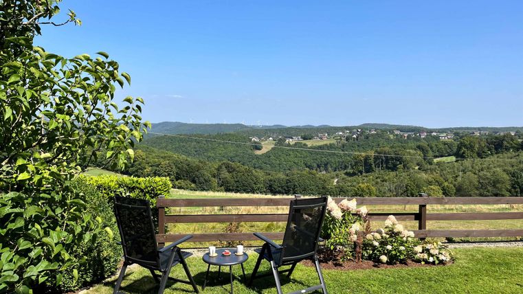 Ein schöner Ausblick auf grüne Hügel von einer Terrasse aus. Zwei Stühle stehen bereit für entspannte Momente in der Natur.