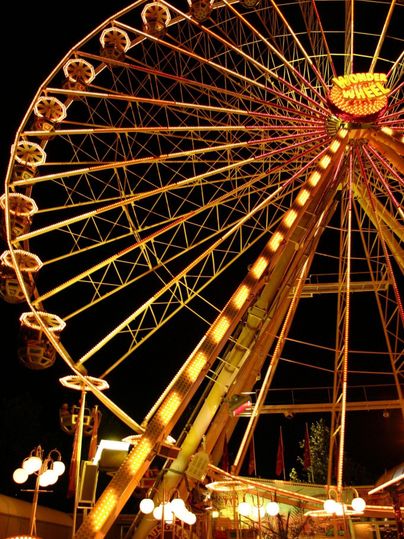 Ein großes Riesenrad leuchtet bunt in der Nacht. Die Lichter strahlen und schaffen eine festliche Atmosphäre.