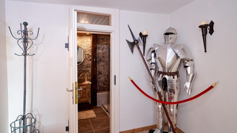 Ein Ritter in voller Rüstung steht an einer Wand neben einer Tür. Der Raum hat helle Wände und einige Wandlampen.