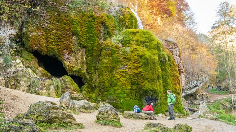 Twee mensen rusten uit bij de met mos bedekte Nohn waterval in de Eifel.