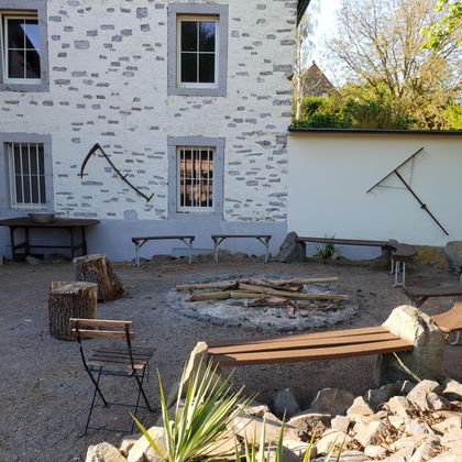 Une cour intérieure confortable avec un foyer et entourée de bancs. Les murs sont simples et il y a quelques outils de décoration.
