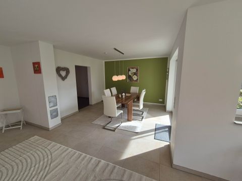 Een moderne eetkamer met een houten tafel en witte stoelen. De muren zijn in zachte kleuren ingericht en er is veel daglicht.
