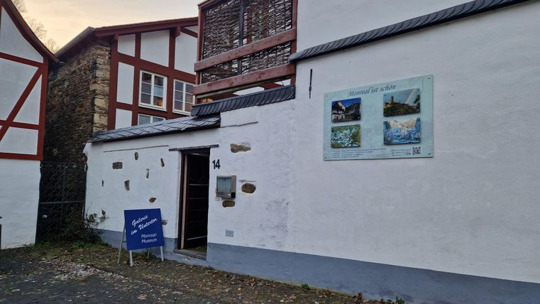 Un bâtiment historique avec des murs blancs et des cadres en bois rouges. Sur le mur se trouve un panneau d'information avec des images des environs.