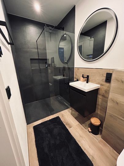 A modern bathroom with clean lines and a large shower. The space is elegant with a round mirror.