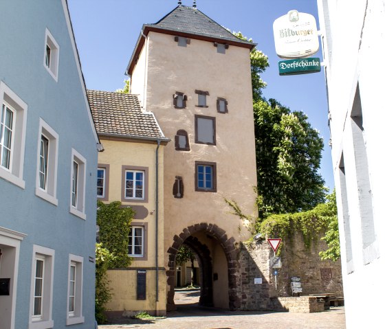 L'Oberes Tor à Dudeldorf, une porte historique de la ville, entourée de maisons colorées et d'une plaque de rue. Journée ensoleillée avec un ciel bleu., © Tourist-Information Bitburger Land_M. Mayer