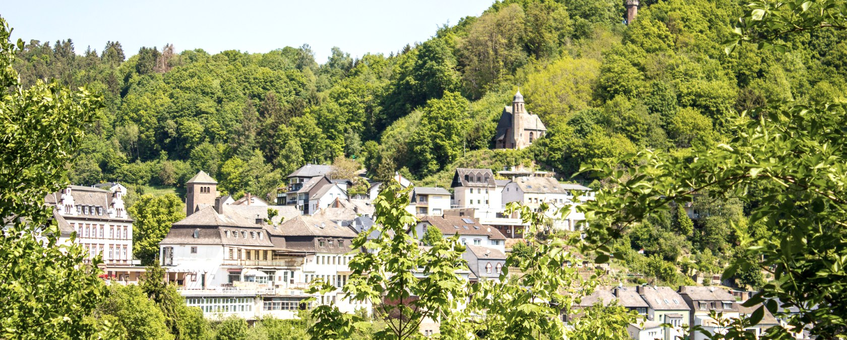 Vue de Kyllburg avec des bâtiments historiques et une église, entourée de collines densément boisées sous un ciel bleu., © Tourist-Information Bitburger Land_Monika Mayer