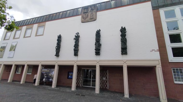 Une façade de bâtiment moderne avec des éléments sculpturaux. Au-dessus de l'entrée se trouve un blason.