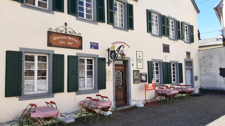 A traditional restaurant with an inviting entrance and green shutters. Outside, there are red chairs and tables, ready for guests.