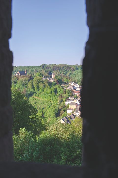 Vue sur un paysage verdoyant avec une église et des maisons, encadrées par des silhouettes sombres.